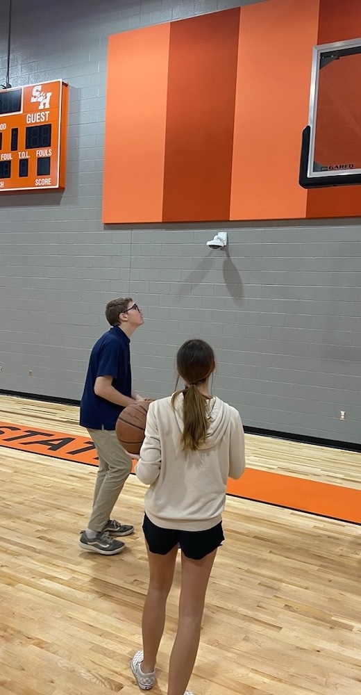 Kassie Van Kampen (right) watches an HISD student shoot a basketball at SAM Camp.