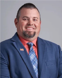 Casey Cox smiles for a photo. Wearing a snappy orange and blue suit.