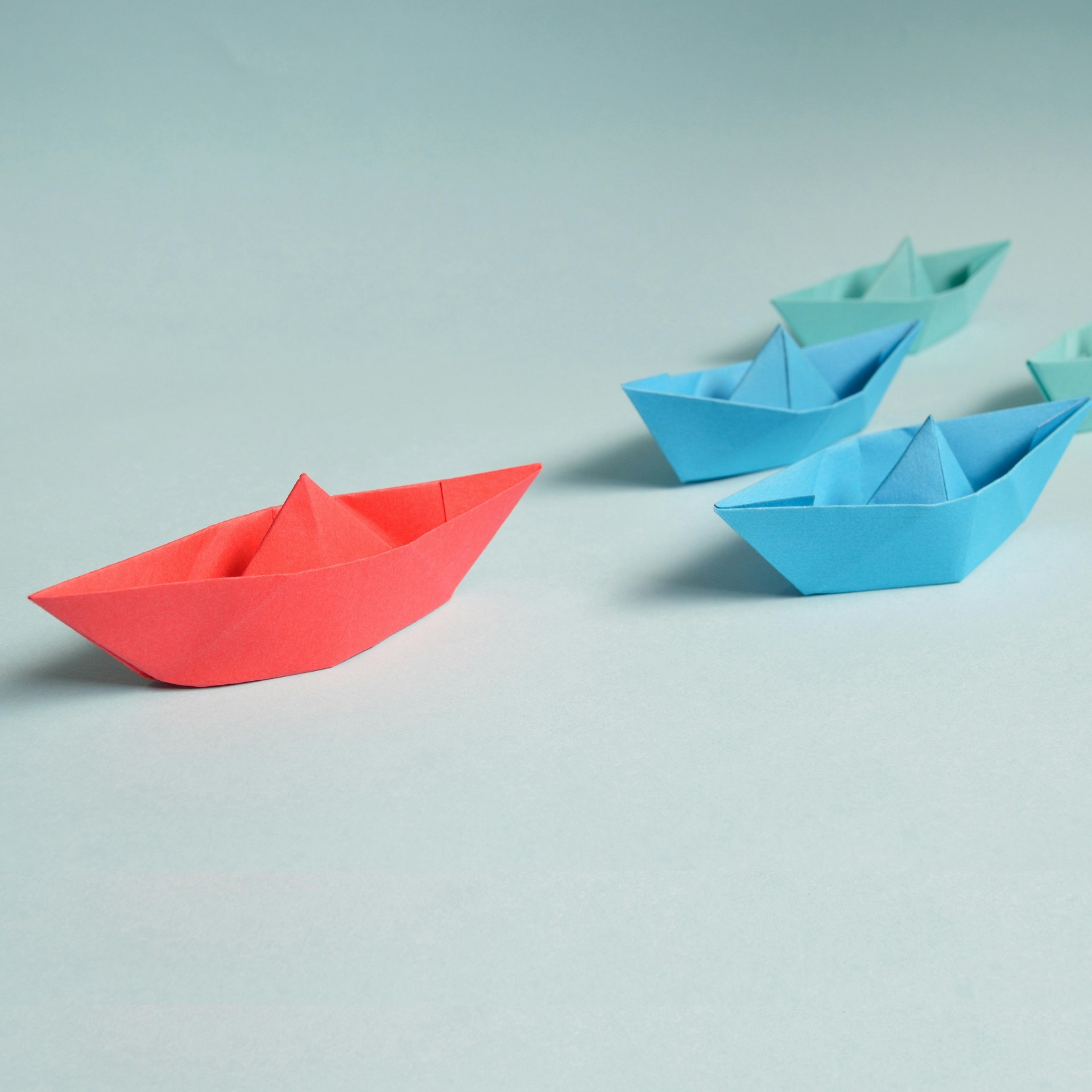 Red paper boat leading blue paper boats